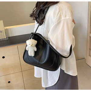 Detail of black leather square tote bag with a white plush bear charm on shoulder