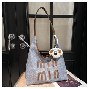 Close-up of blue textured tote bag with brown letter patch and plush dog charm accessory