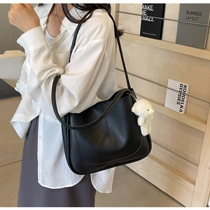 Close-up of black U-shaped shoulder bag with matte leather finish and white bear charm