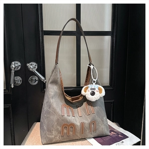 Detail view of large tote bag in grey suede texture with brown leather straps and plush charm