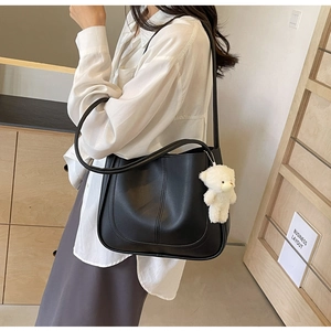 Detail of black PU leather shoulder bag with white bear charm and stylish stitched patterns