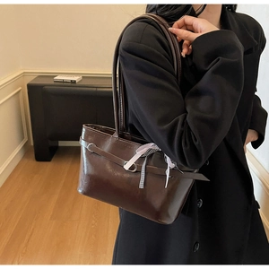 Dettaglio della borsa a spalla marrone lucida con nastro a righe chic e fibbia metallica