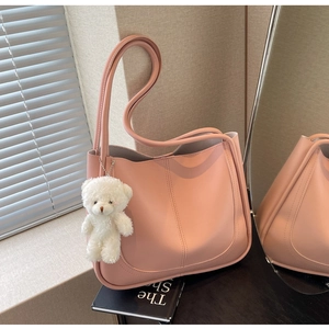 Detail of pink square shoulder bag with plush bear charm on minimalist leather texture