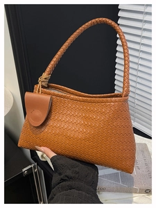 Dettaglio di una borsa sottobraccio intrecciata marrone con manico largo e trama in pelle
