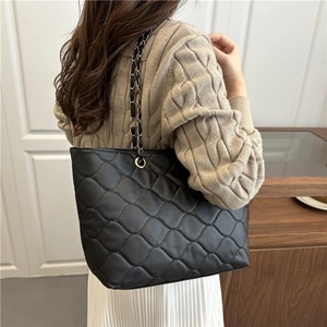 Grand cabas noir matelassé avec bandoulière chaîne dorée porté sur un pull en maille