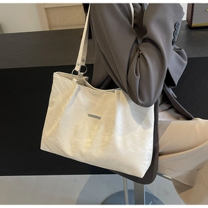 Close-up of textured white tote bag with metallic logo plate and silver rings
