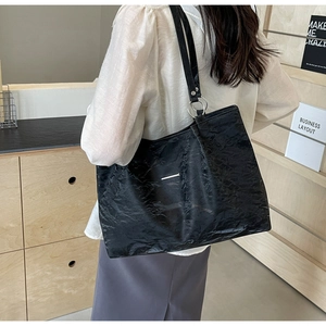 Detail of black pleated tote bag with silver metal ring connectors on a model shoulder