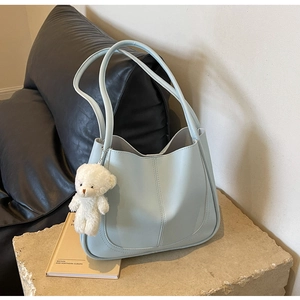 Detail of light blue faux leather tote bag with white plush bear charm on stone