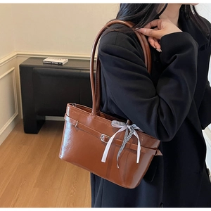 Detail van een bruine leren shopper met een decoratieve zwart-witte geruite strik als accent