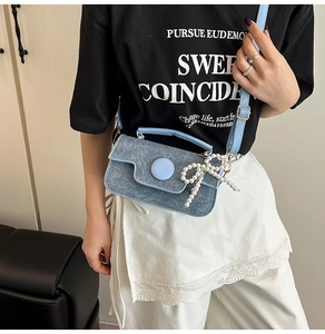 Détail du sac bandoulière en denim bleu avec boucle en résine et nœud en perles blanches