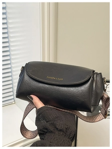 Détail d'un sac bandoulière en cuir noir avec une large bandoulière à motifs tissés