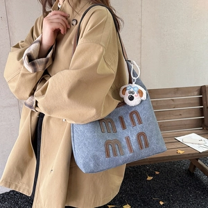 Blue denim hobo tote bag with letter patch and plush puppy charm on a model shoulder