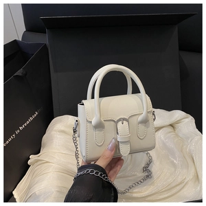Close-up of minimalist off-white square bag with silver metal chain on satin background