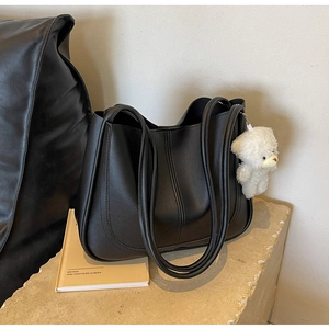 Close-up of black leather tote bag with white plush bear charm on stone pedestal
