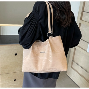 Close-up of beige pleated leather tote bag showing metallic detail and silver metal ring