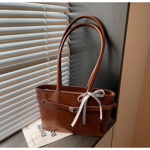Dettaglio borsa sottobraccio marrone lucido con fibbia decorativa e fiocco a scacchi