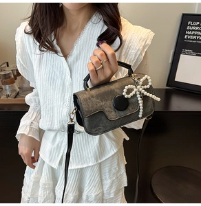 Détail du sac bandoulière gris texturé avec pendentif nœud en perles et bouton noir