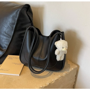 Close-up of a black tote bag with vertical stitching and a cute plush bear charm