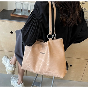 Close-up of beige tote bag showing pleated texture, metal logo, and silver ring details