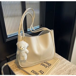 Chic cream leather tote bag with plush bear charm displayed on a photography book