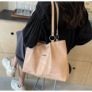 Detail of beige tote bag showing textured pleats and silver metallic ring hardware