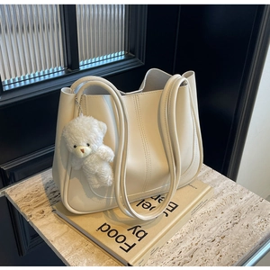 Detail of a beige faux leather tote bag with vertical stitching and a plush bear charm