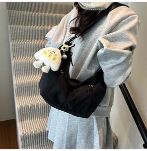 Close-up of black canvas dumpling bag with a cute plush monster charm on a gray outfit