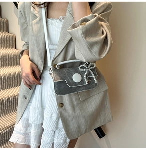 Détail du sac bandoulière gris avec bordure en cuir blanc et pendentif perle