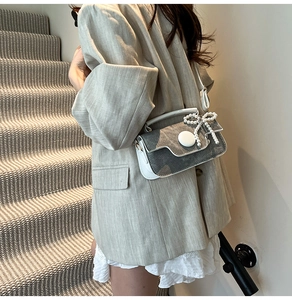 Détail du sac bandoulière en denim gris avec charm perle porté sur un blazer beige