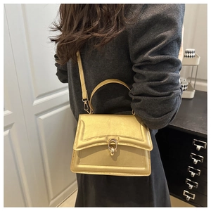 Detail of golden structured handbag featuring a unique circular metal clasp and fine stitching