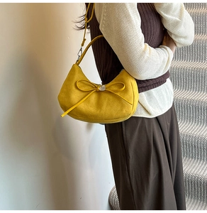 Detail of yellow crescent bag with suede texture, bow knot, and silver heart metal charm