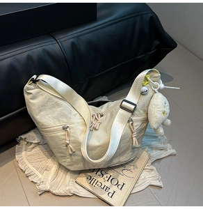 Detail of cream nylon dumpling bag with wide adjustable strap and plush puppy charm