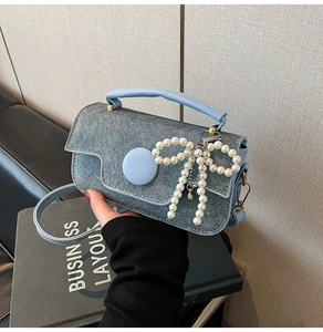 Gros plan d'un sac à main en denim bleu clair avec breloque nœud en perles et détail rond