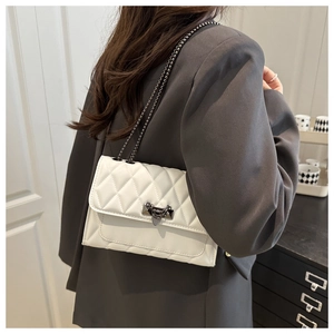 Detail of white quilted crossbody bag with metal buckle and chain strap on a blazer