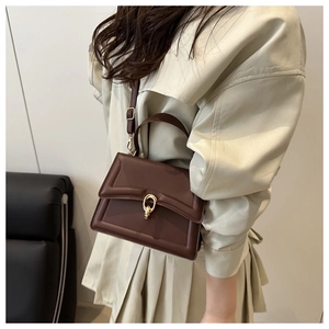 Detail of dark brown leather crossbody bag with gold chain buckle and textured pattern