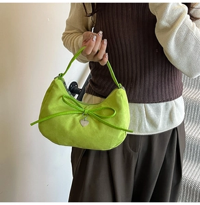 Detail of neon green suede crescent bag with leather bow and silver heart pendant