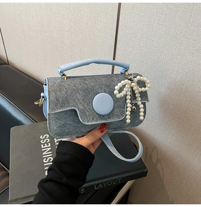 Détail d'un sac à main en denim gris avec poignée en cuir bleu clair et pendentif nœud perlé