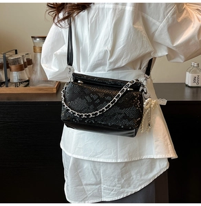 Close-up of black snake pattern square bag with silver chain and pearl charm detail