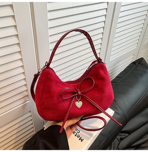 Detail of red velvet hobo bag with a soft bow and silver heart pendant on a leather sofa