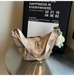 Detail of khaki nylon crescent bag with wide strap and cute plush charm on a metal table