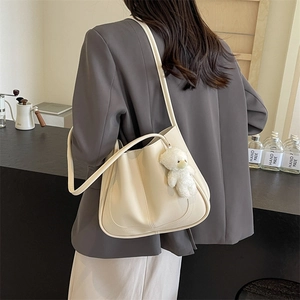 Minimalist creamy white leather shoulder bag with plush bear charm worn by a model