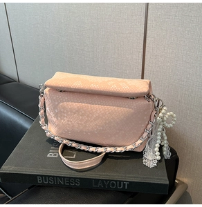 Detail of pink snake-pattern handbag with pearl bow charm and metal chain strap