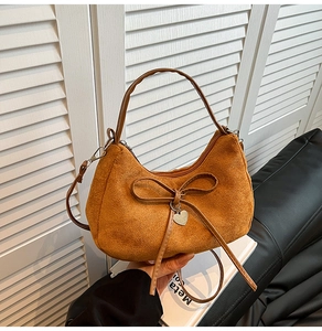 Detail of caramel suede crescent bag featuring a bow knot and heart-shaped metal pendant