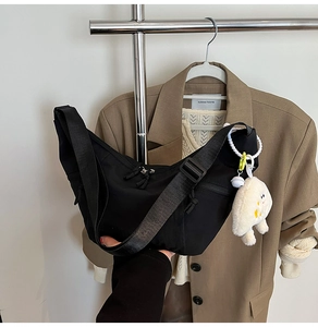 Detail of black nylon dumpling bag with adjustable strap and cute white plush charm