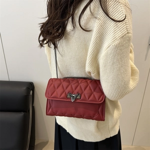 Deep red quilted crossbody bag with heart lock on a cream sweater lifestyle view