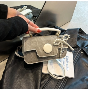 Détail d'un sac en jean gris avec poignée en cuir blanc et breloque en perles