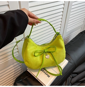 Detail of neon green dumpling bag with bow decor and a heart-shaped metal pendant