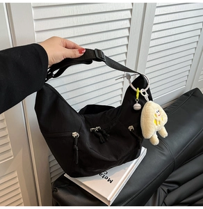 Detail of black nylon dumpling bag with yellow plush charm and adjustable strap