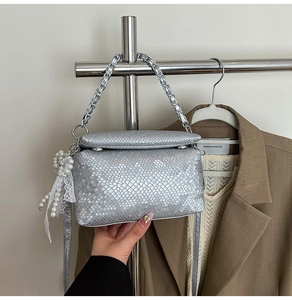Detail of silver snake-pattern bag with metal chain handle and pearl lace pendant