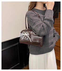 Detail of dark brown leather tote featuring a pearl bow and lace pendant accessory